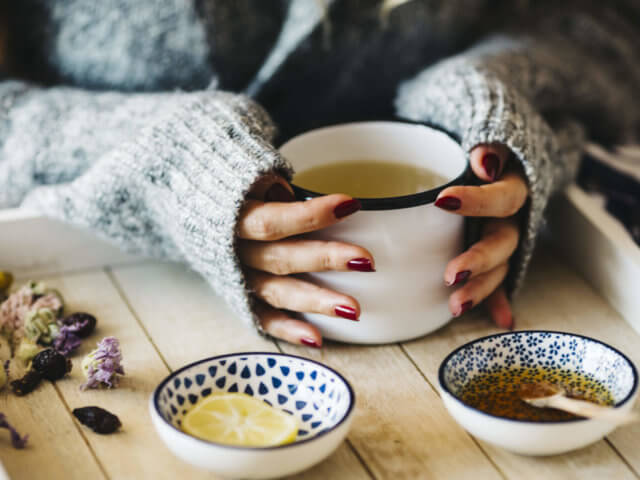 A female model is drinking herbal tea for flu, she is pouring herbal tea into a white enamel cup