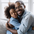 Loving African father in glasses hugs little daughter, family sitting on couch cuddling closed eyes enjoy sincere moment of tenderness, feeling bond express appreciation and gratitude for love concept