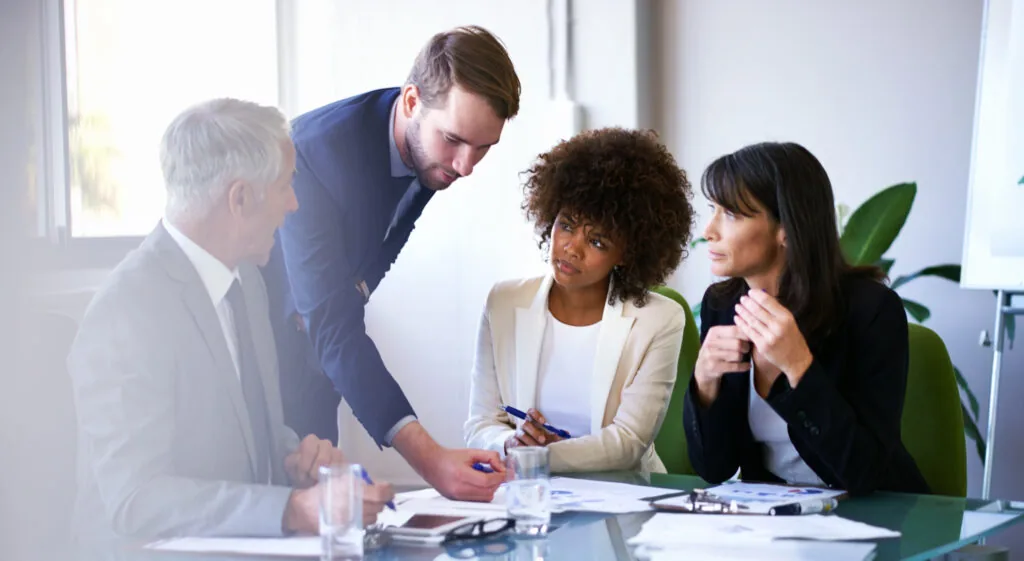 Four colleagues reviewing printed charts during an office meeting.