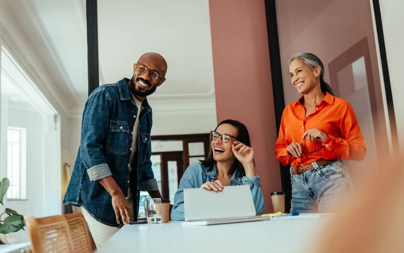 Group of creatives and freelancers enjoying collaboration in a modern, colorful office boardroom with a joyful team member.