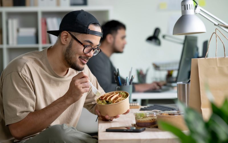 Young Asian man eating healthy meal while working, Businessman having a lunch break at the office