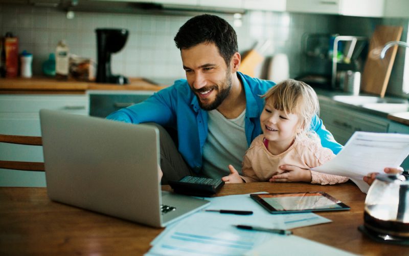 Single father using the laptop with his young daughter in his lap