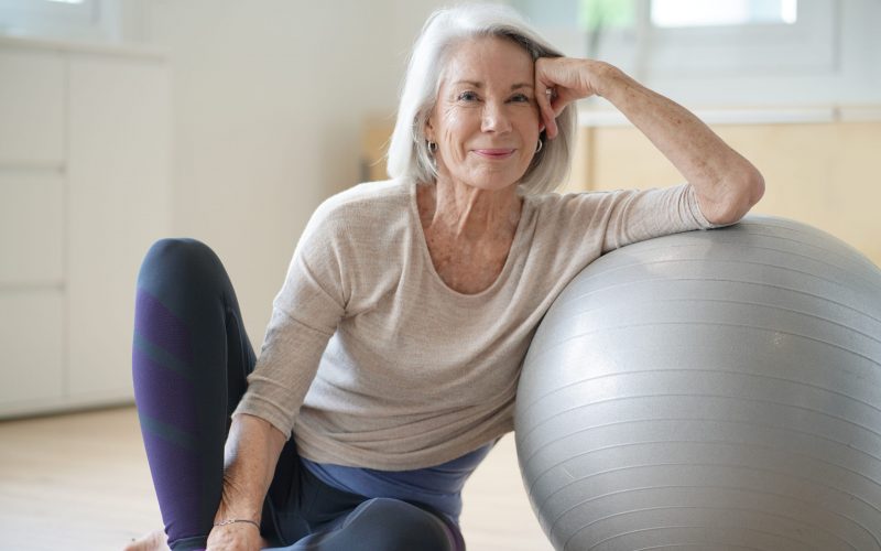 Smiling elderly woman resting on a swiss ball at home