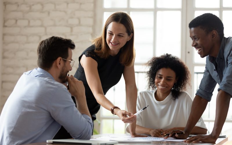 Caucasian woman team leader mentor teach staff multiethnic workers at corporate group briefing explain work results analyzing financial report together, planning project, brainstorming process concept