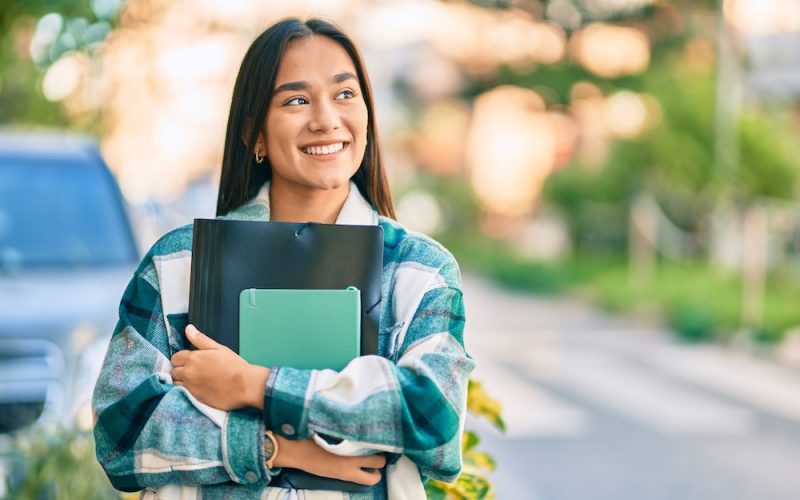 Young latin student girl smiling happy holding folder at the city.