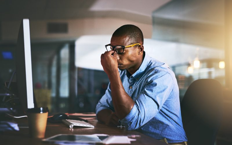 Black business man, stress and headache in night, office and fatigue by computer for project deadline. African businessman, burnout or anxiety in workplace by pc, web design startup and mental health.