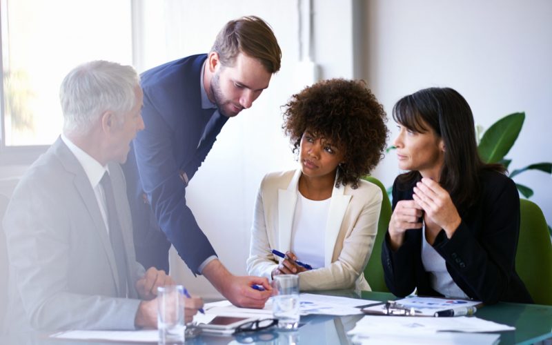 Four colleagues reviewing printed charts during an office meeting.